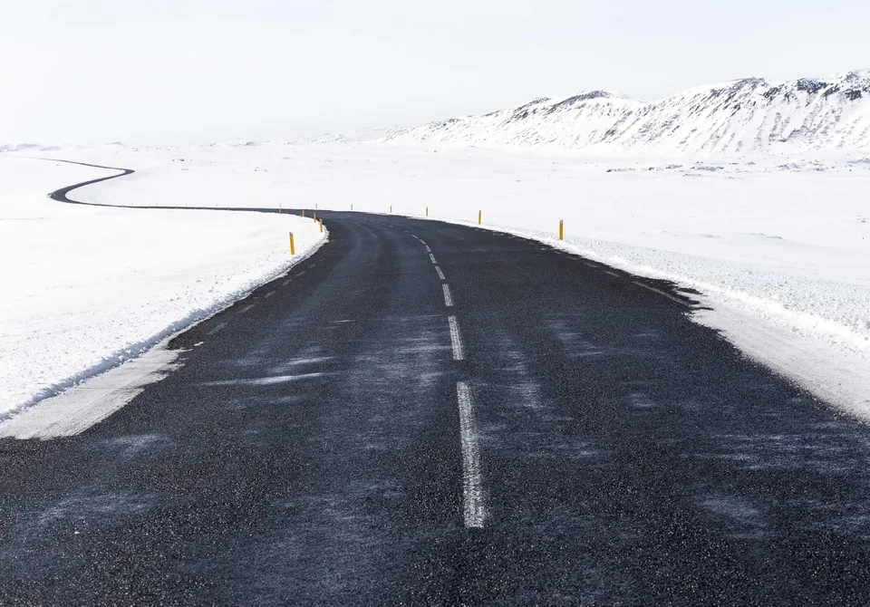 Karla kaplı ovada kıvrılarak uzaklaşan ıslak asfalt yol